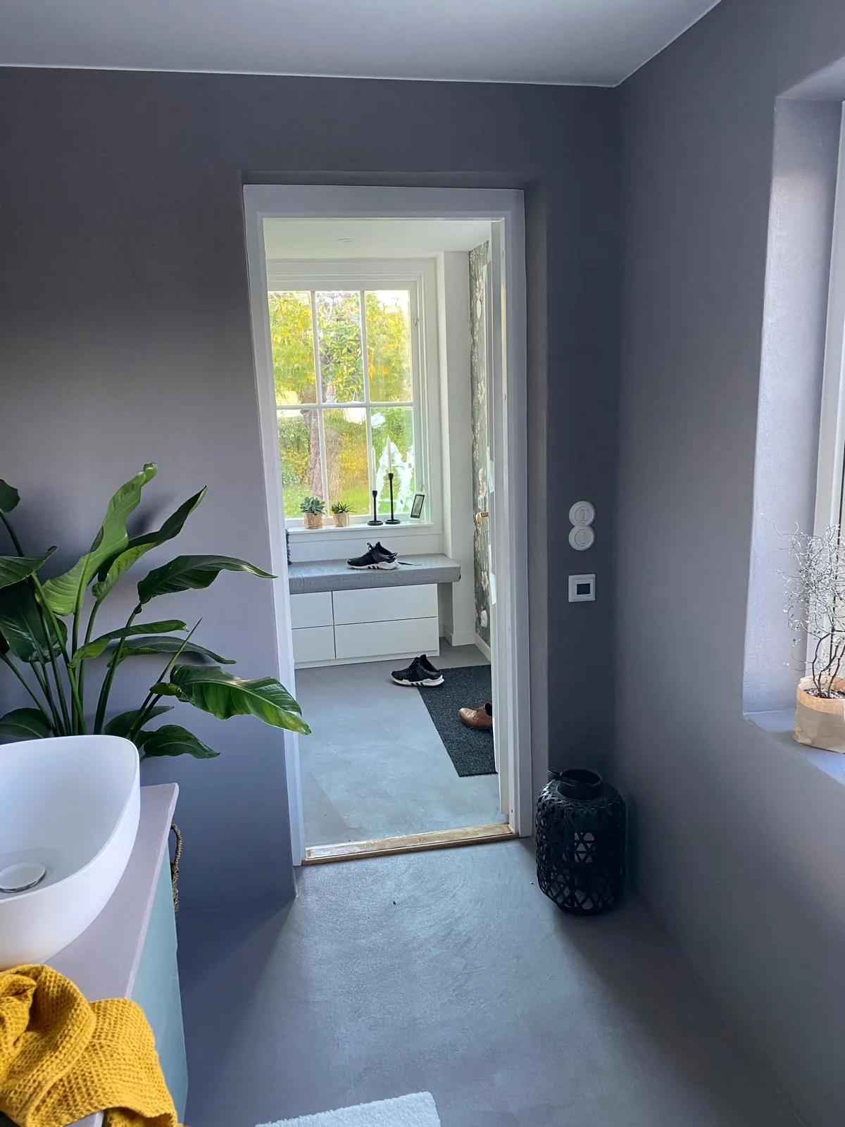 Ferdig bad i grått med servant, planter og åpen dør ut mot gangen.