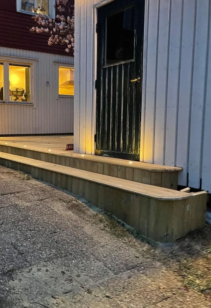 Inngangsparti i tre om kvelden, med lys i trappetrinnene.